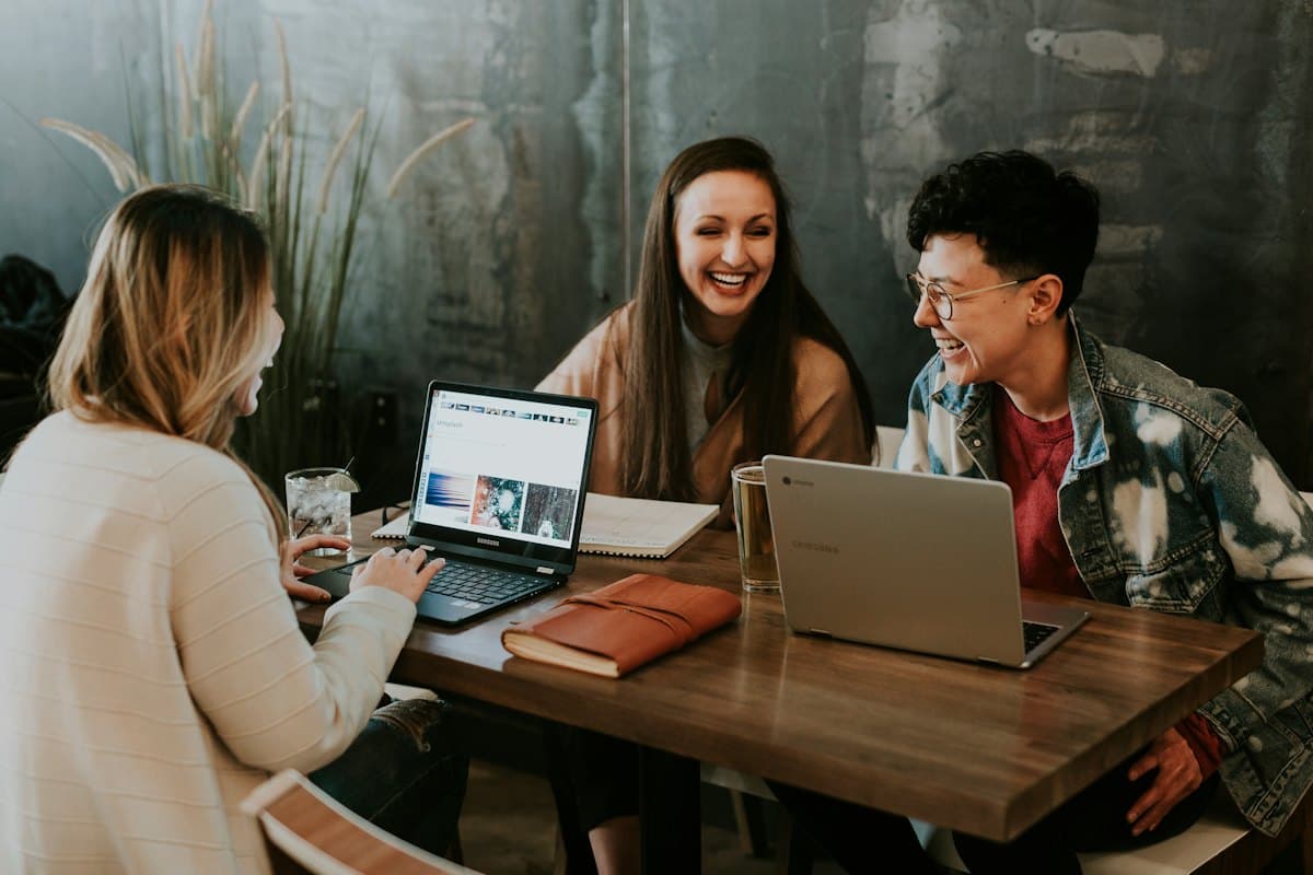 Three colleagues laughing around a table with laptops and coffee